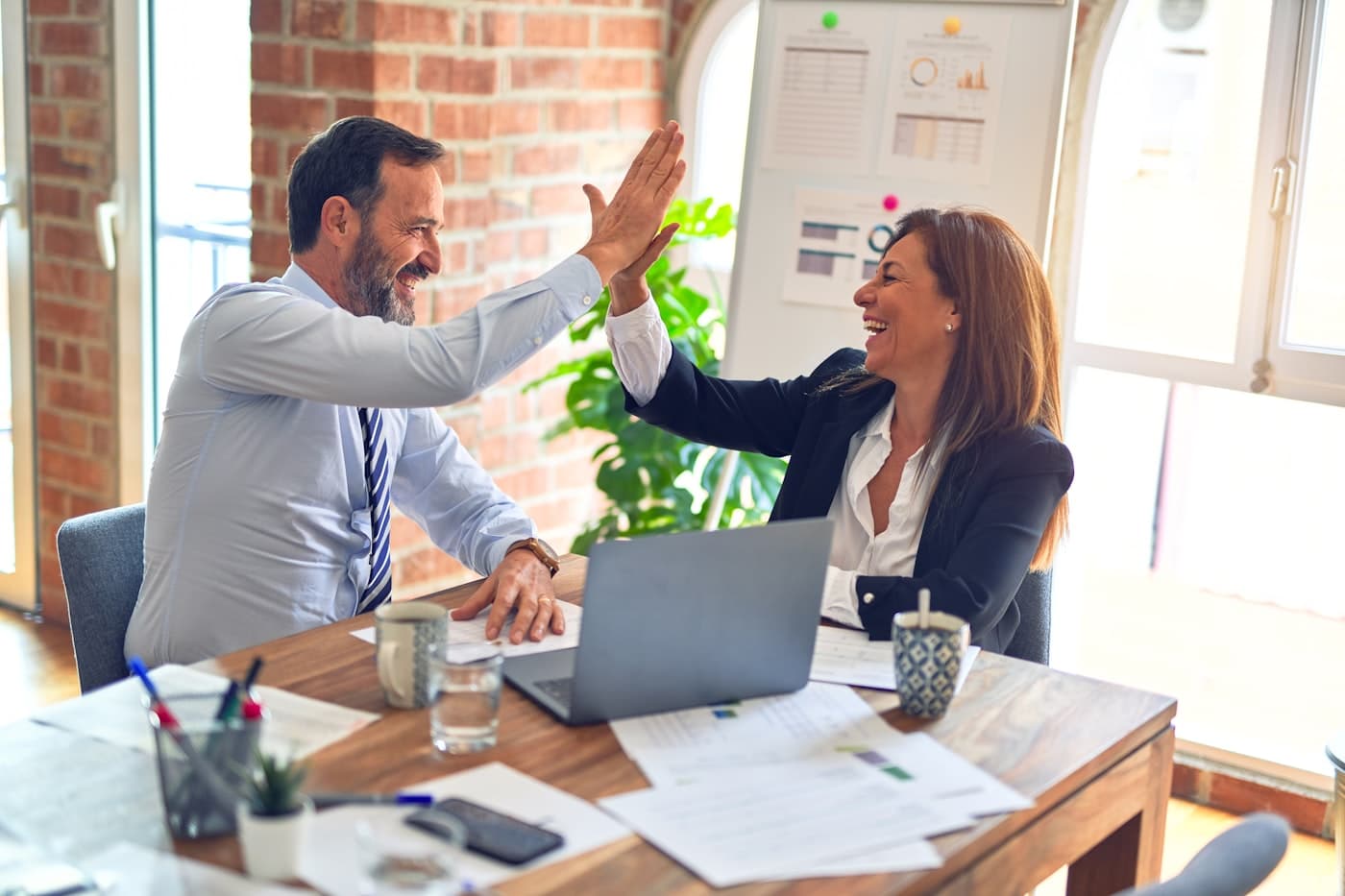 Two people celebrating a signed agreement across a desk of paperwork